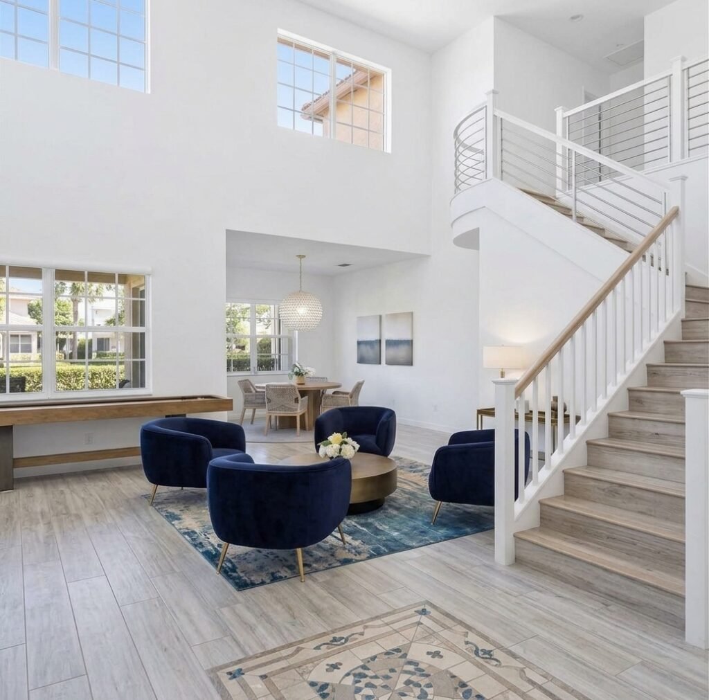A sunlit living area with tall windows, an open staircase, and seamless flow between living and dining spaces.