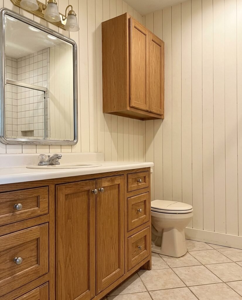 A bathroom vanity finished in natural wood tones with a large frameless mirror and updated fixtures.