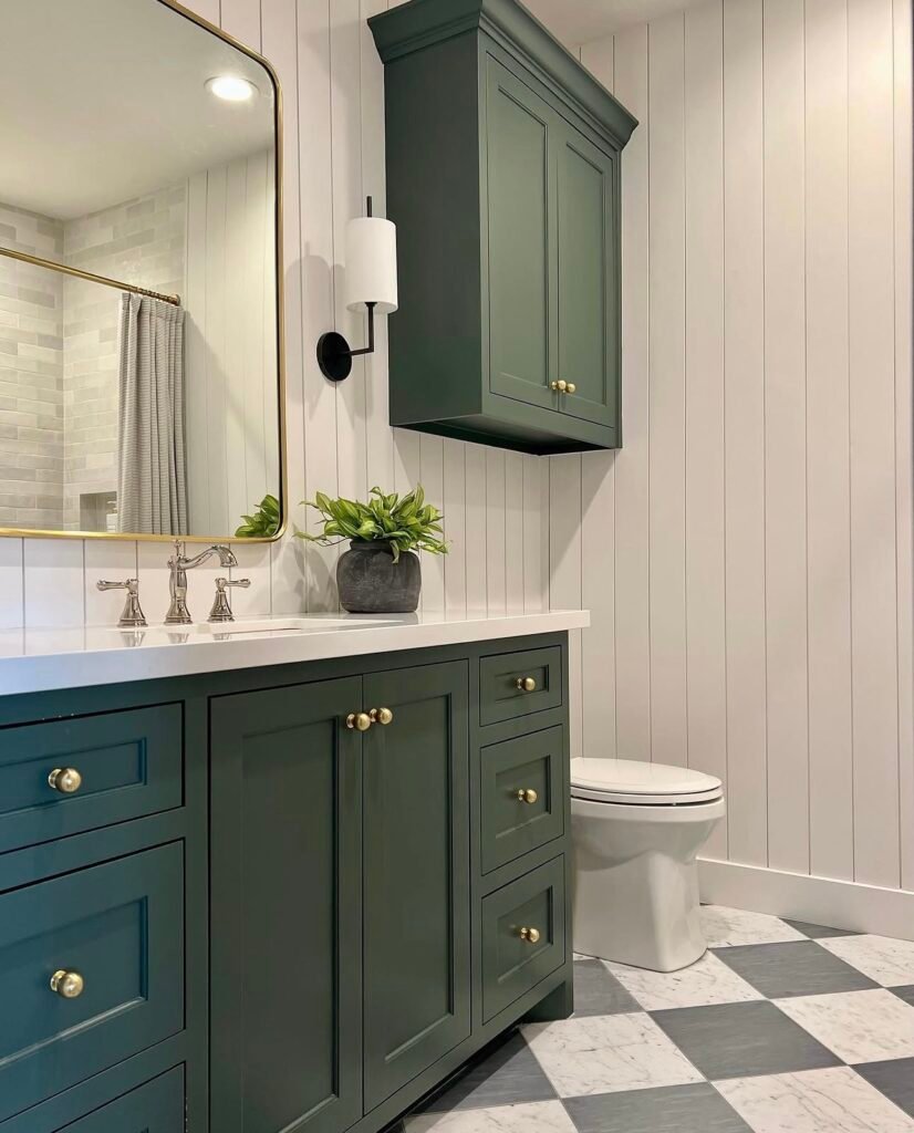 A forest-green shaker-style vanity with brass hardware, white shiplap walls, and a black-and-white checkered tile floor.